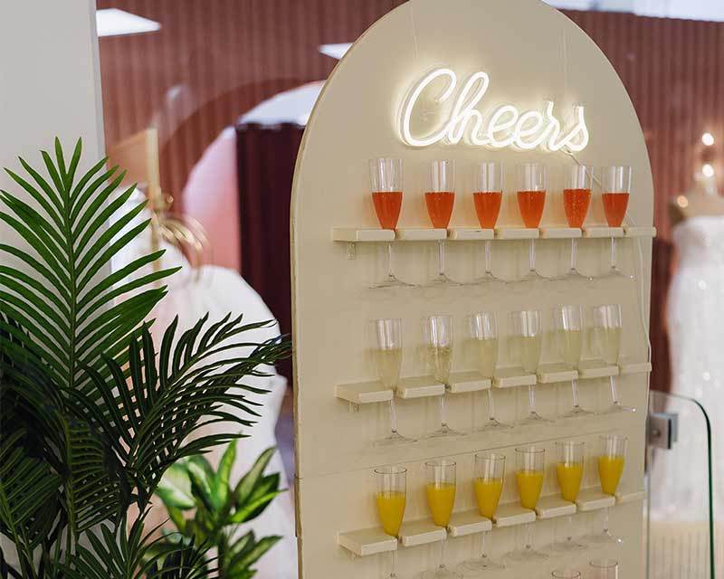 Moderner Getränkeaufsteller mit "Cheers" Schriftzug und gefüllten Champagnergläsern.